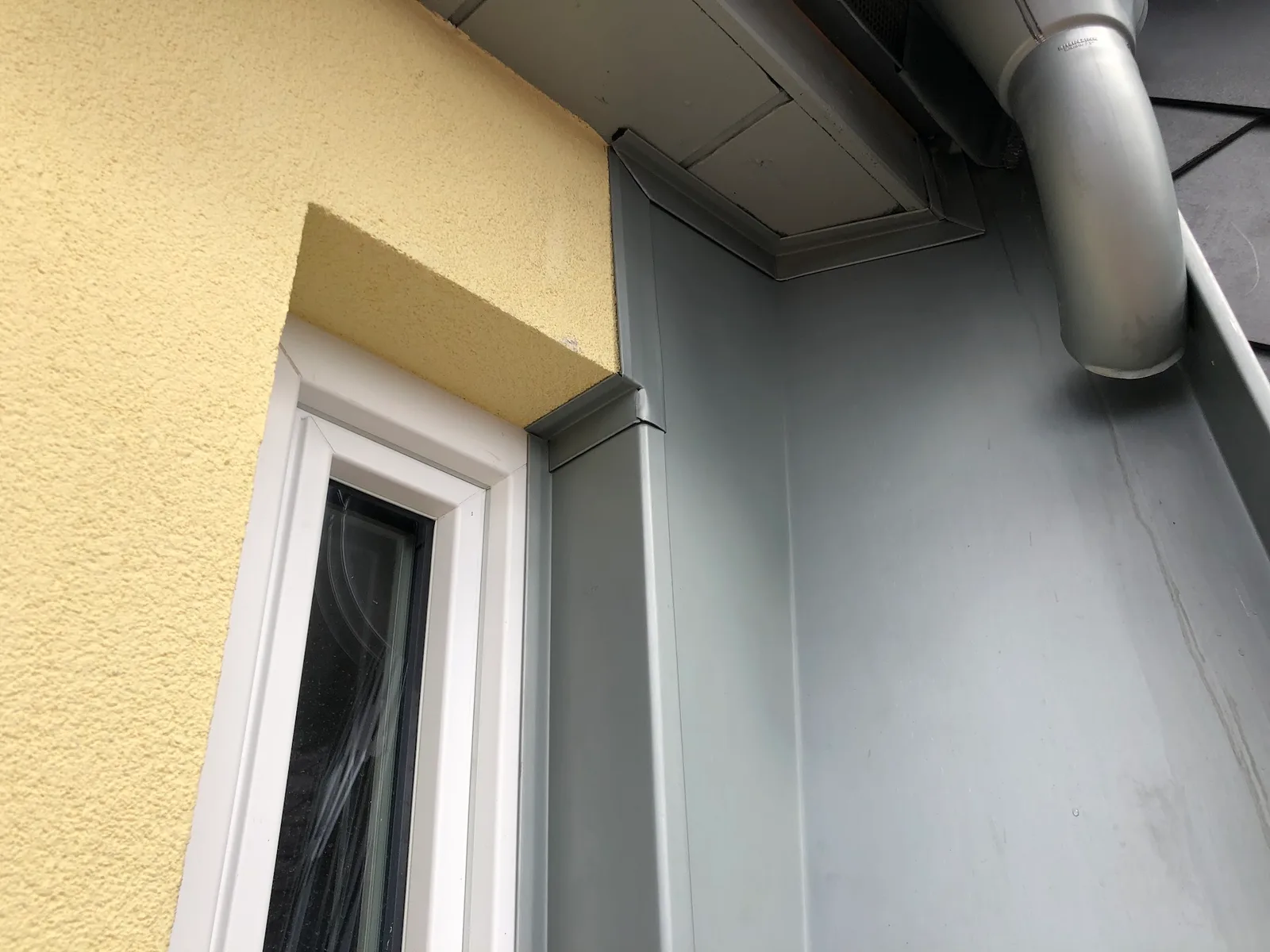 Fertige Blecharbeit an einer Fensterlaibung, daneben ein Fallrohr mit der eingeprägten Aufschrift RHEINZINK